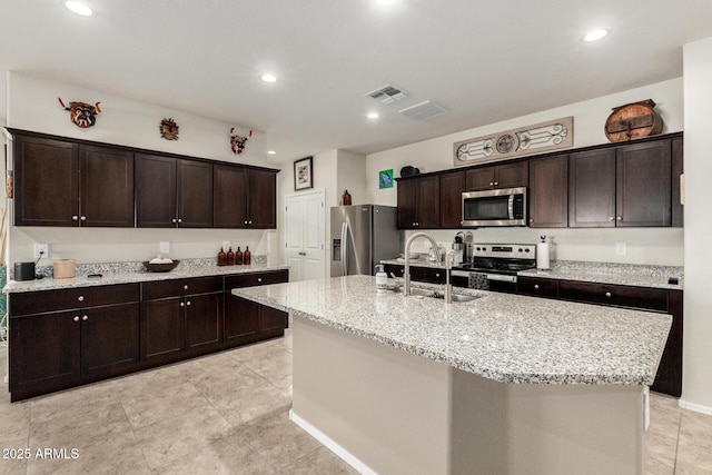 kitchen with stainless steel appliances, visible vents, dark brown cabinetry, a sink, and an island with sink