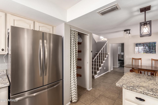 kitchen featuring stainless steel refrigerator, light stone countertops, hanging light fixtures, and dark tile patterned floors