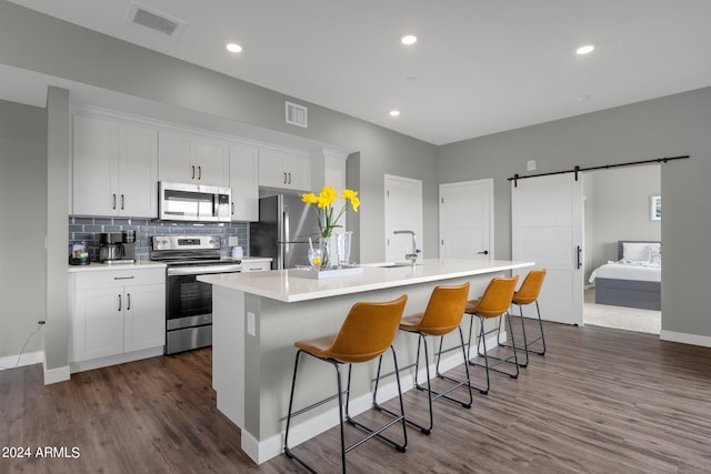 kitchen with dark hardwood / wood-style floors, a barn door, stainless steel appliances, a breakfast bar area, and an island with sink