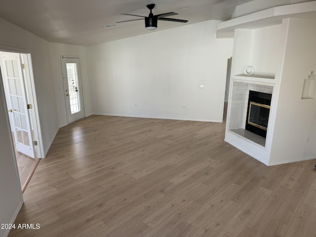 unfurnished living room featuring a tiled fireplace, ceiling fan, and light hardwood / wood-style flooring