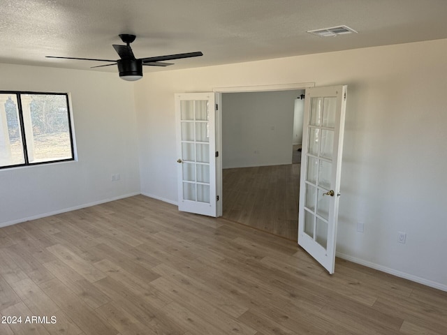 empty room featuring ceiling fan, light wood-type flooring, a textured ceiling, and french doors