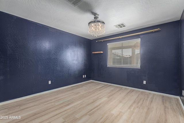 spare room with light hardwood / wood-style floors, a textured ceiling, and an inviting chandelier