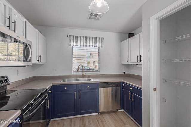 kitchen featuring light wood-type flooring, stainless steel appliances, sink, blue cabinetry, and white cabinets