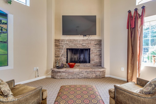 living room featuring carpet flooring, a stone fireplace, and baseboards