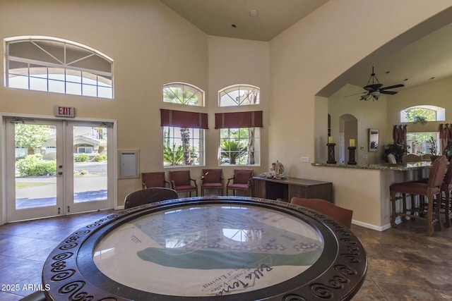 interior space featuring french doors, baseboards, ceiling fan, and a towering ceiling