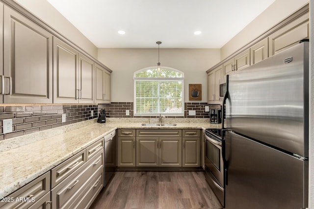 kitchen featuring dark wood finished floors, light stone counters, decorative backsplash, stainless steel appliances, and a sink