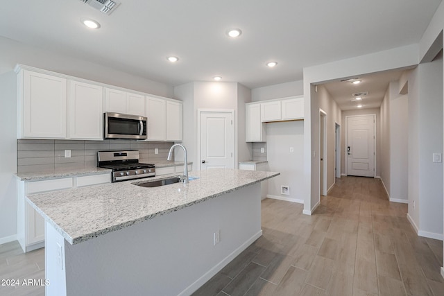 kitchen with white cabinetry, sink, stainless steel appliances, light hardwood / wood-style flooring, and a center island with sink