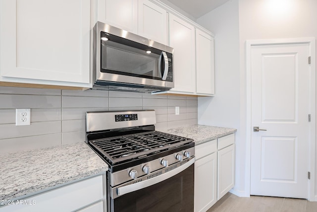 kitchen featuring backsplash, light stone countertops, appliances with stainless steel finishes, light hardwood / wood-style floors, and white cabinetry