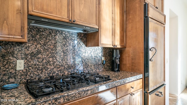 kitchen featuring paneled refrigerator, black gas cooktop, tasteful backsplash, dark stone counters, and exhaust hood