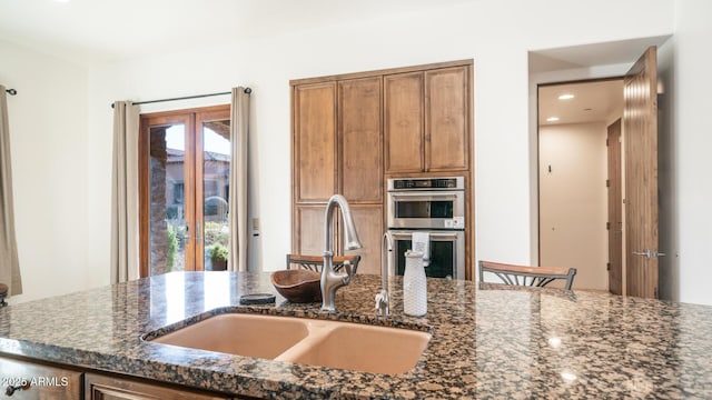 kitchen with sink, dark stone counters, and stainless steel double oven