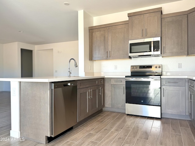 kitchen with a peninsula, appliances with stainless steel finishes, wood finish floors, and light countertops