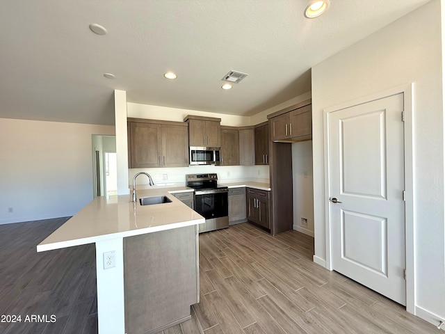 kitchen with stainless steel appliances, light countertops, light wood-style flooring, a sink, and a peninsula