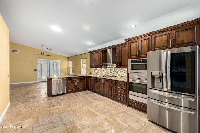 kitchen with wall chimney range hood, a ceiling fan, vaulted ceiling, baseboards, and stainless steel appliances