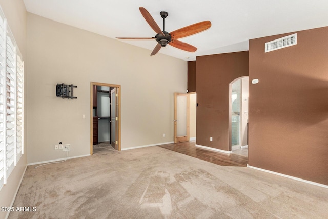 empty room with carpet flooring, arched walkways, high vaulted ceiling, a ceiling fan, and visible vents