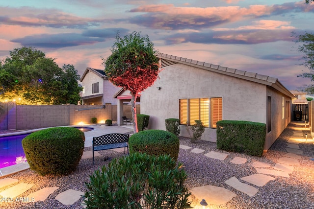 back of house at dusk with a fenced in pool, a fenced backyard, a patio area, and stucco siding