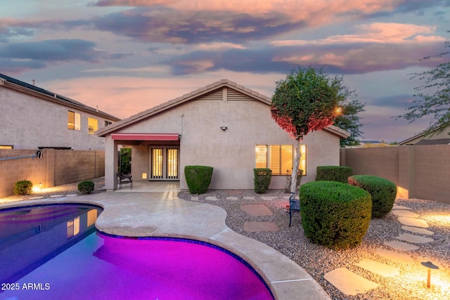 back of property at dusk featuring a fenced backyard, a fenced in pool, stucco siding, and a patio area