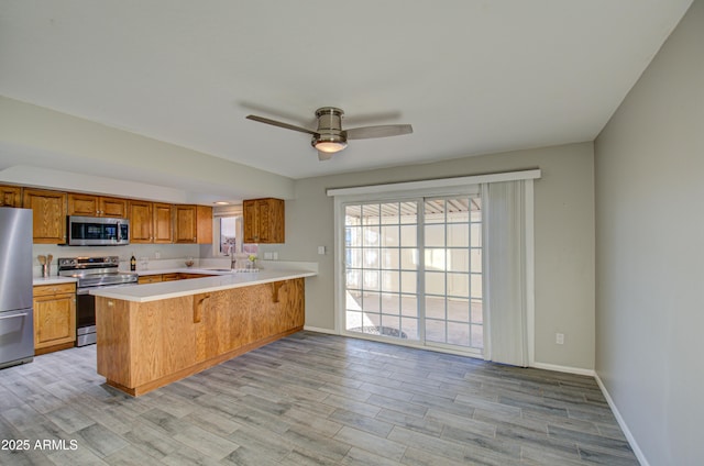 kitchen featuring ceiling fan, stainless steel appliances, kitchen peninsula, a kitchen bar, and light wood-type flooring