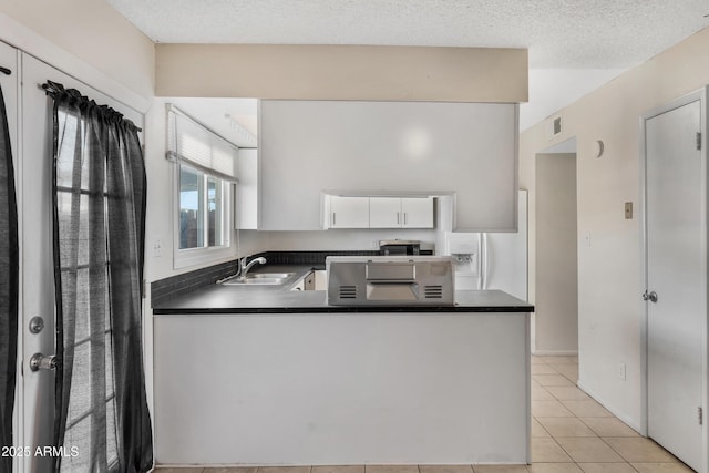 kitchen featuring light tile patterned flooring, white cabinetry, sink, kitchen peninsula, and a textured ceiling