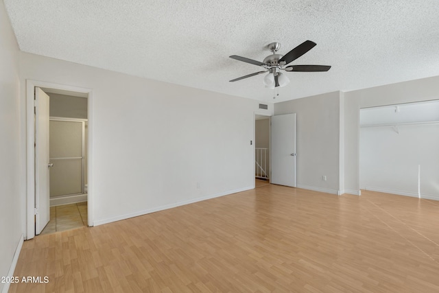 unfurnished bedroom featuring ceiling fan, light hardwood / wood-style floors, a textured ceiling, ensuite bath, and a closet