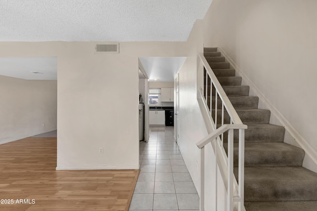 stairway with tile patterned flooring, sink, and a textured ceiling