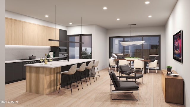 kitchen with light brown cabinets, an island with sink, light hardwood / wood-style flooring, hanging light fixtures, and a kitchen breakfast bar