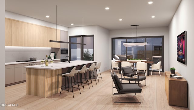 kitchen with a center island with sink, hanging light fixtures, light hardwood / wood-style floors, and a breakfast bar