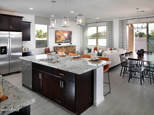 kitchen featuring stainless steel appliances, a kitchen island with sink, sink, pendant lighting, and a notable chandelier