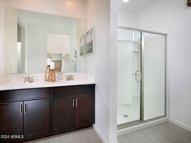 full bath featuring double vanity, a shower stall, baseboards, and a sink