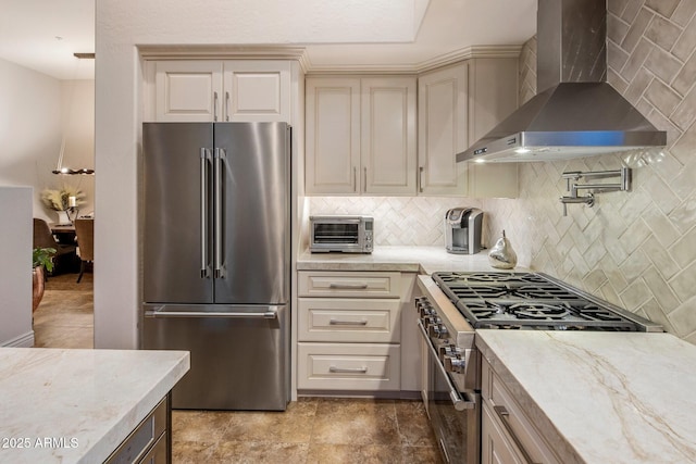 kitchen with appliances with stainless steel finishes, wall chimney exhaust hood, cream cabinets, and decorative backsplash