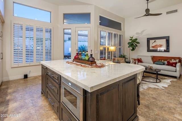 kitchen featuring stainless steel microwave, dark brown cabinetry, ceiling fan, a kitchen island, and open floor plan