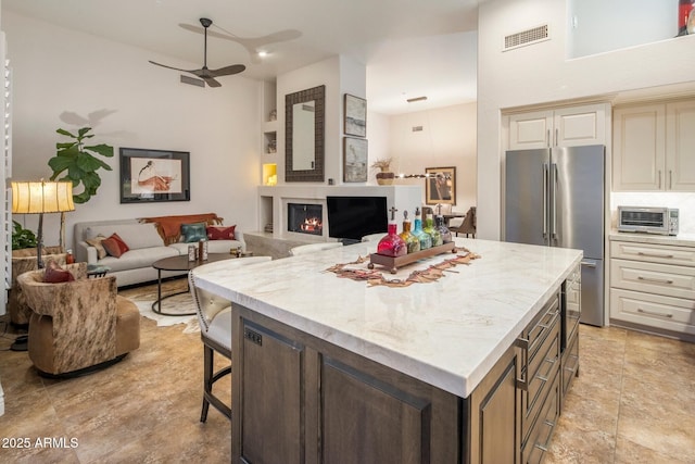 kitchen with high quality fridge, ceiling fan, open floor plan, a kitchen island, and a breakfast bar