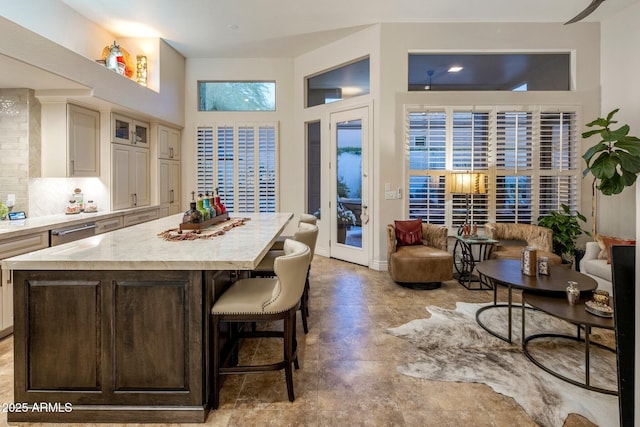 kitchen with a breakfast bar, stainless steel dishwasher, glass insert cabinets, a center island, and backsplash