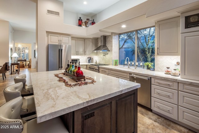kitchen with high quality appliances, wall chimney exhaust hood, tasteful backsplash, light stone counters, and recessed lighting
