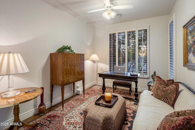 living area featuring a ceiling fan, baseboards, a desk, and wood finished floors