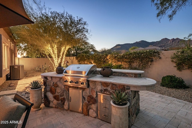 view of patio / terrace featuring area for grilling, exterior kitchen, cooling unit, a mountain view, and a fenced backyard