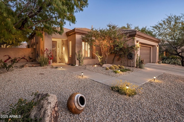 view of front facade featuring driveway, stucco siding, an attached garage, and fence