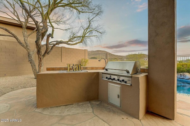 patio terrace at dusk featuring sink, an outdoor kitchen, and grilling area