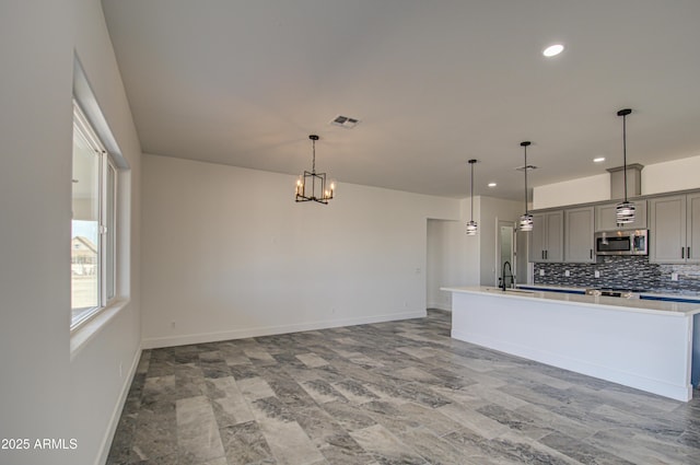 kitchen featuring gray cabinetry, an island with sink, decorative backsplash, pendant lighting, and sink