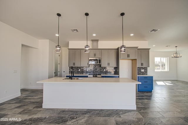 kitchen with appliances with stainless steel finishes, sink, a kitchen island with sink, and decorative light fixtures