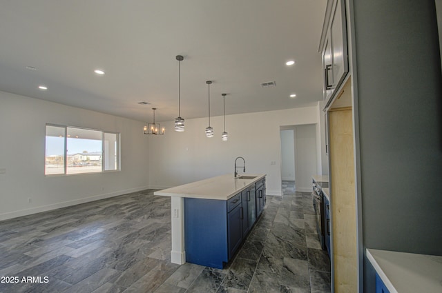 kitchen with blue cabinetry, an island with sink, decorative light fixtures, sink, and an inviting chandelier