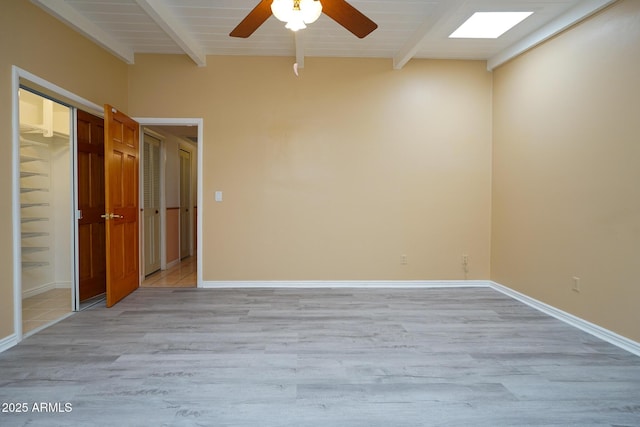 empty room with baseboards, beam ceiling, ceiling fan, and light wood finished floors