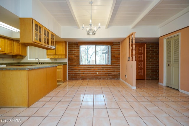 kitchen with dark countertops, brick wall, glass insert cabinets, an inviting chandelier, and light tile patterned flooring