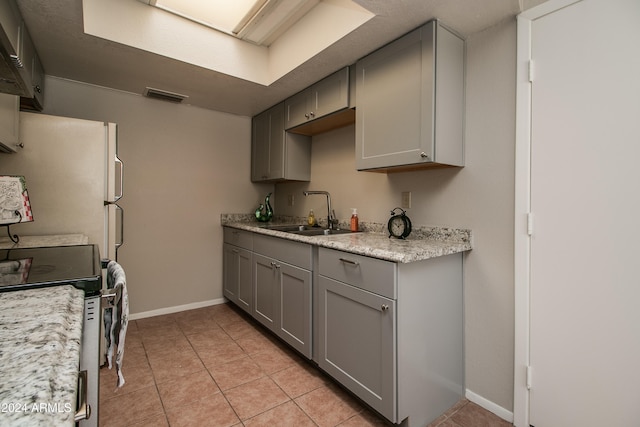 kitchen with gray cabinetry, stove, light tile patterned floors, and sink