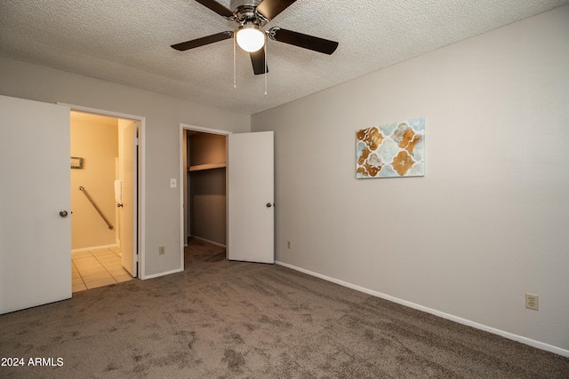 unfurnished bedroom featuring a spacious closet, a closet, ceiling fan, and light carpet