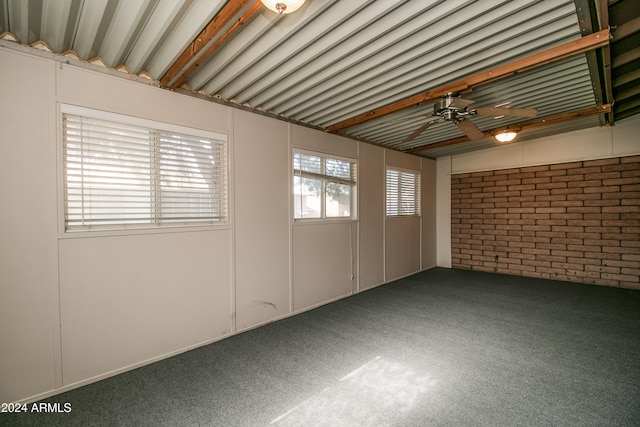 carpeted spare room featuring ceiling fan, a wealth of natural light, and brick wall