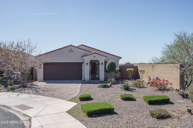 mediterranean / spanish-style house featuring decorative driveway, a tile roof, stucco siding, an attached garage, and fence