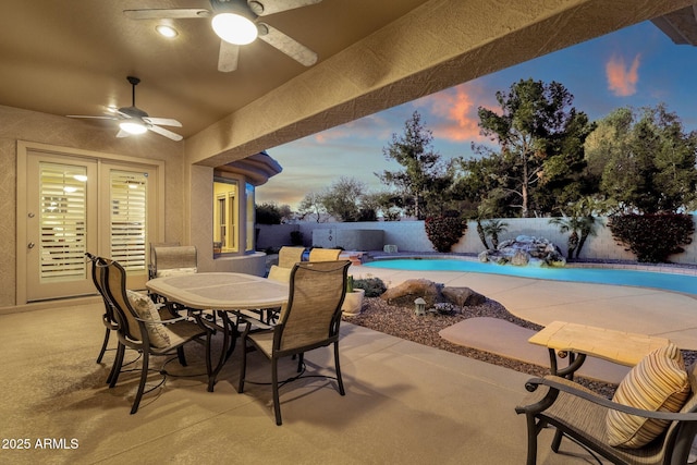 patio terrace at dusk with ceiling fan and a fenced in pool