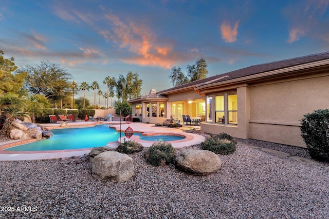 pool at dusk featuring an in ground hot tub and a patio