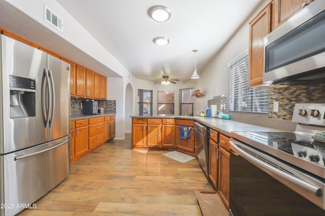 kitchen featuring appliances with stainless steel finishes, tasteful backsplash, hanging light fixtures, kitchen peninsula, and light hardwood / wood-style flooring