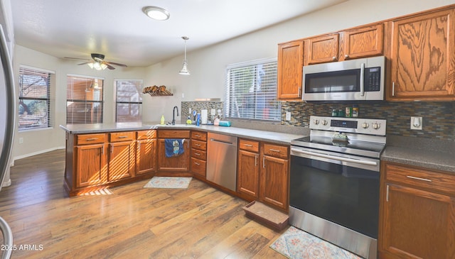 kitchen with decorative light fixtures, sink, light hardwood / wood-style floors, kitchen peninsula, and stainless steel appliances